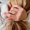 Mano de mujer tocándose el cabello con anillo de oro en forma de pluma