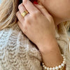 Mujer con mano con anillo de pluma dorada y pulsera de perlas