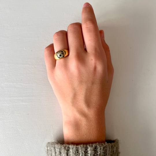 Mano de mujer con anillo sello dorado y piedra natural jaspe cebra