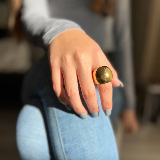 Mano de mujer con anillo grande de acero dorado en forma de bola