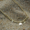 Collar de cadena barbada gruesa dorada con 3 colgantes en forma de corazón sobre la arena