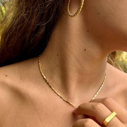 Escote de mujer con collar de prismas dorado, anillo minimalista y pendiente de aro