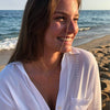 Mujer sonriendo en la playa con un collar con inicial dorado