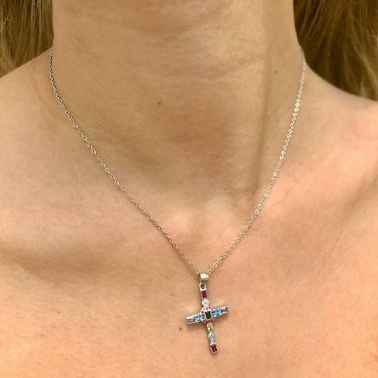 Escote de mujer con collar de plata y colgante de cruz con piedras de colores