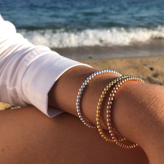 Brazo de mujer junto a la playa con tres pulseras de bolas de plata