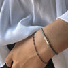 Mano de mujer con pulsera de cadena negra y pulsera de cordón gris con bolitas de plata