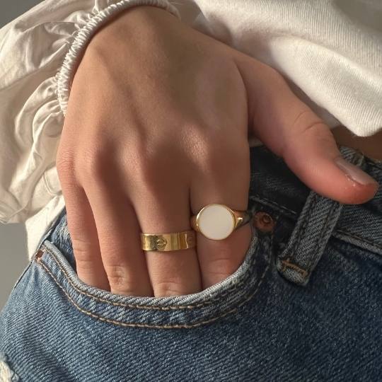 Mano con anillo sello blanco y anillo dorado metiendo el bolsillo en un pantalón