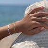 Mano de mujer con pulsera de cadena de serpiente dorada sobre sombrero de playa 
